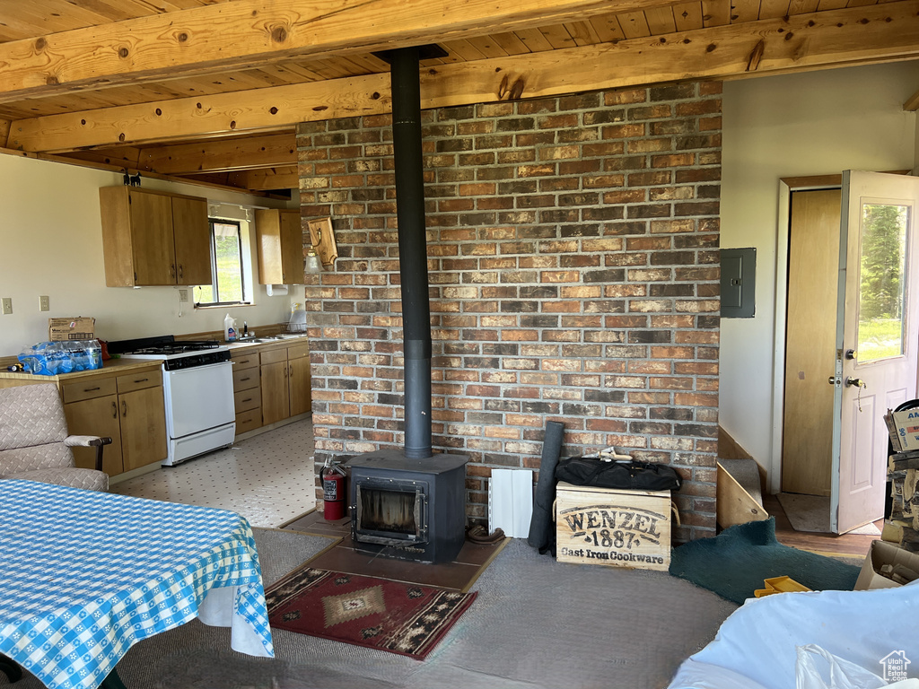 Kitchen with gas range gas stove, a wood stove, a wood ceiling with exposed beams, electric panel, and light floors