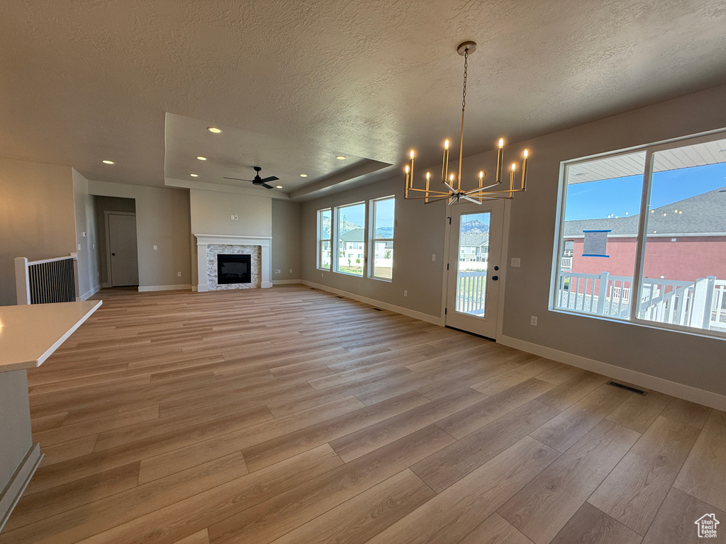 Unfurnished living room with a textured ceiling, light wood-style flooring, a ceiling fan, a chandelier, and recessed lighting