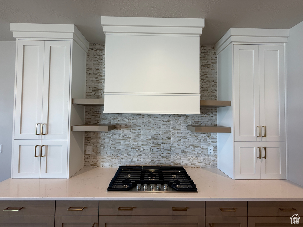 Kitchen with open shelves, stainless steel gas stovetop, backsplash, light stone countertops, and range hood