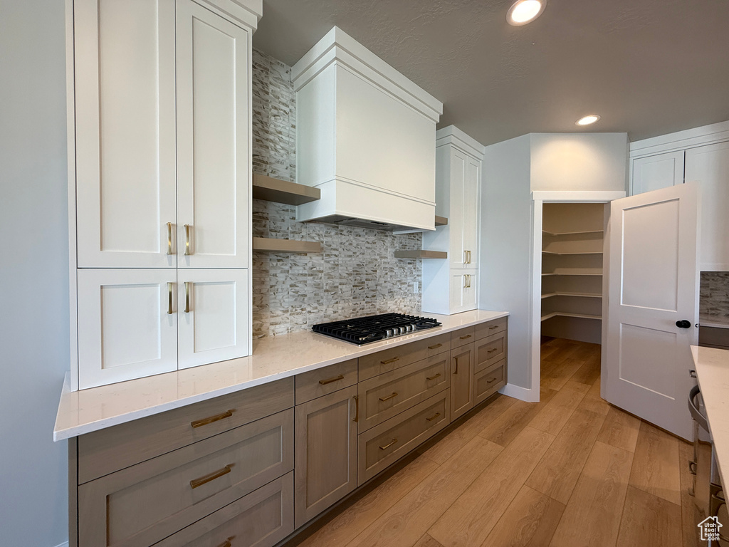 Kitchen with stainless steel gas stovetop, light wood-style flooring, gray cabinets, open shelves, and backsplash