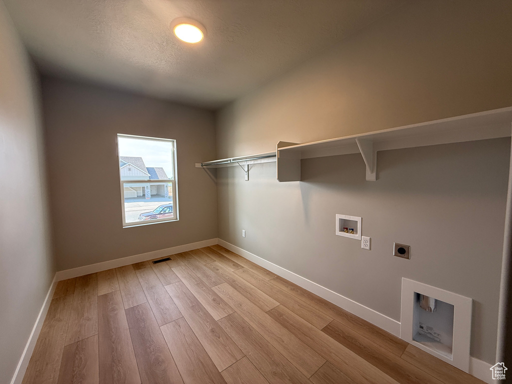 Laundry area featuring electric dryer hookup, hookup for a washing machine, light wood-style flooring, and a textured ceiling