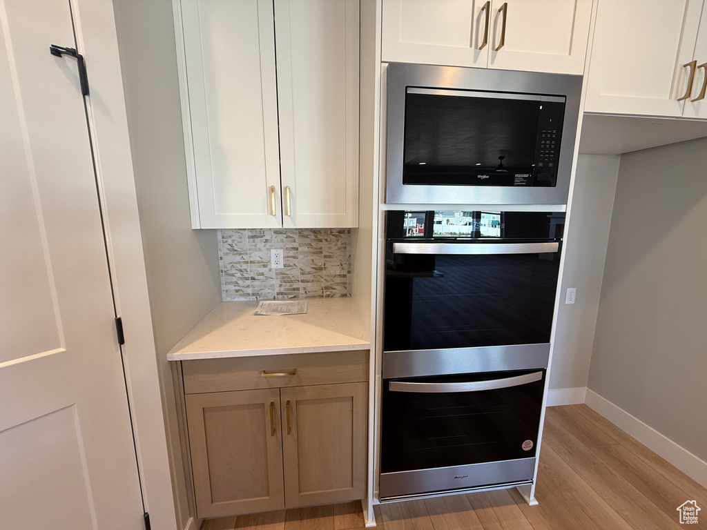 Kitchen featuring stainless steel appliances, tasteful backsplash, light wood finished floors, light stone countertops, and white cabinetry