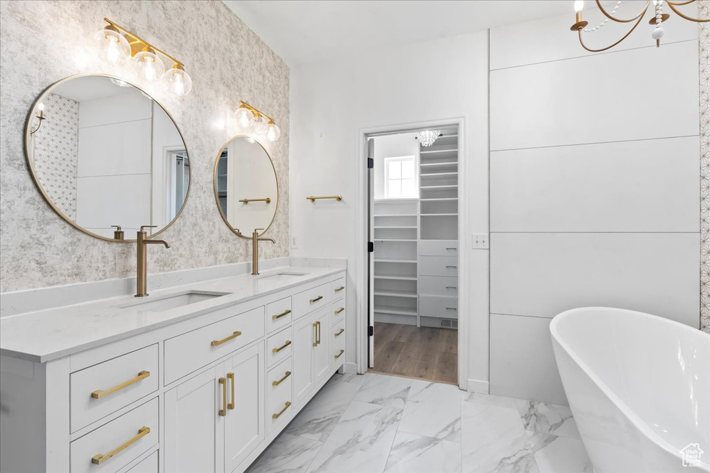 Bathroom with a chandelier, double vanity, a freestanding bath, marble look tile flooring, and a walk in closet