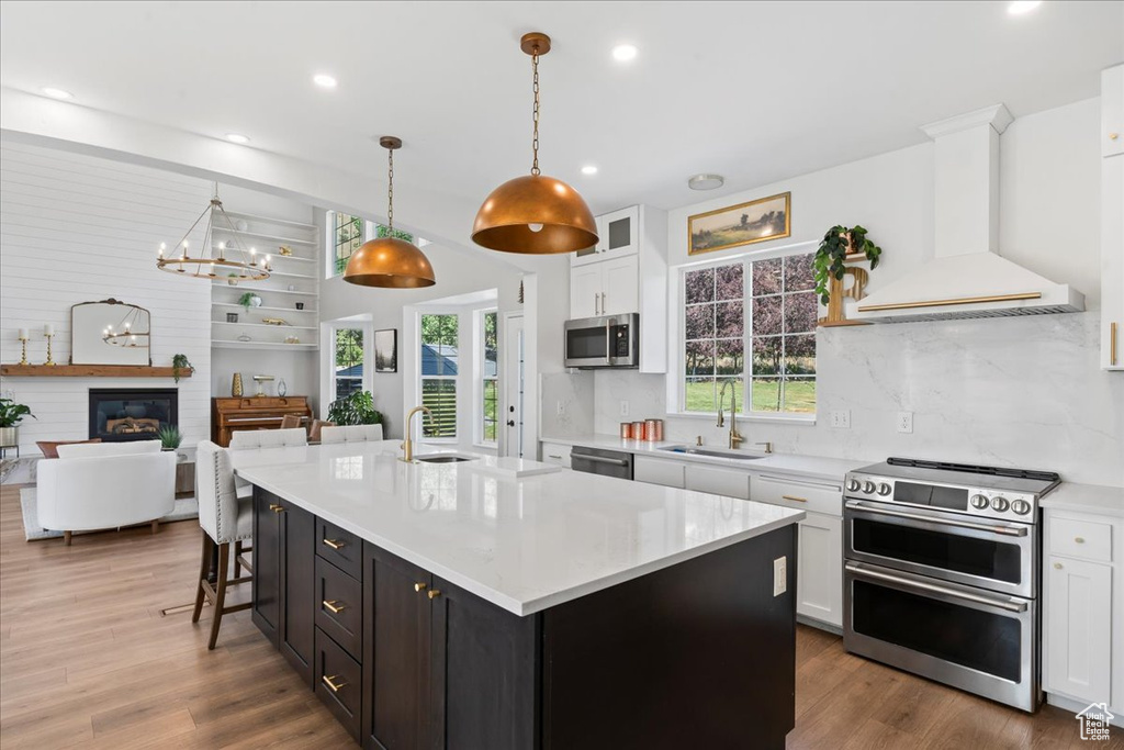 Kitchen with stainless steel appliances, premium range hood, white cabinetry, light countertops, and wood finished floors