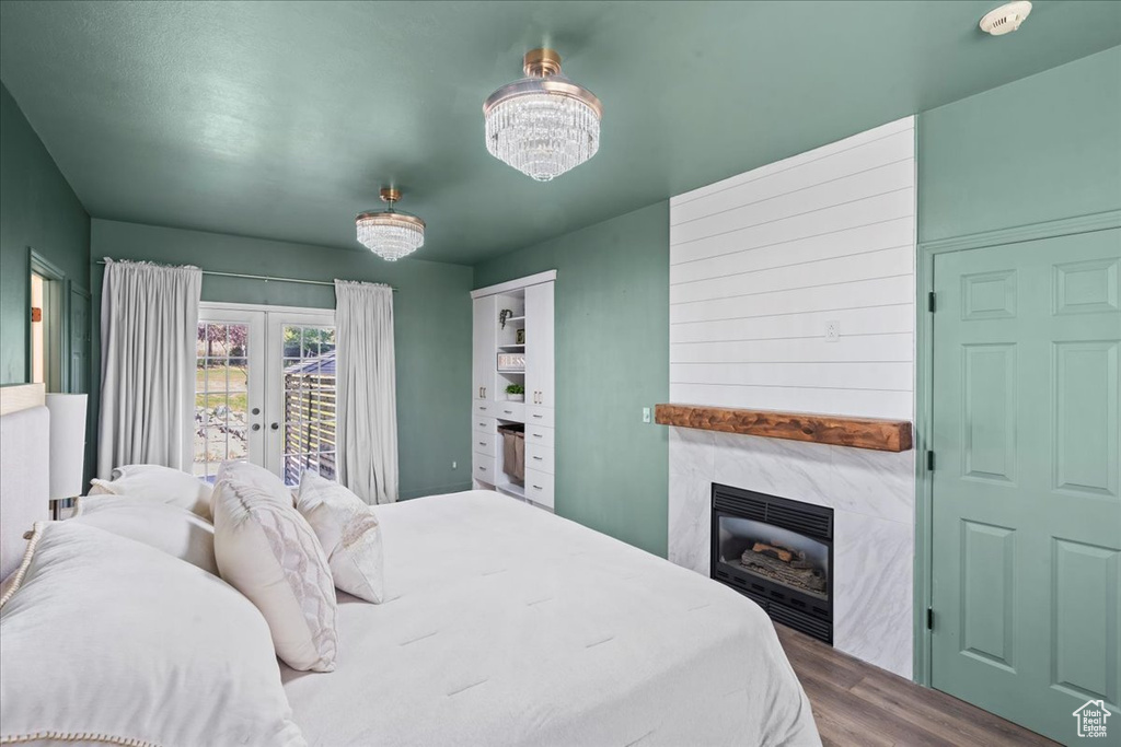 Bedroom featuring wood finished floors, a fireplace, access to exterior, a chandelier, and french doors