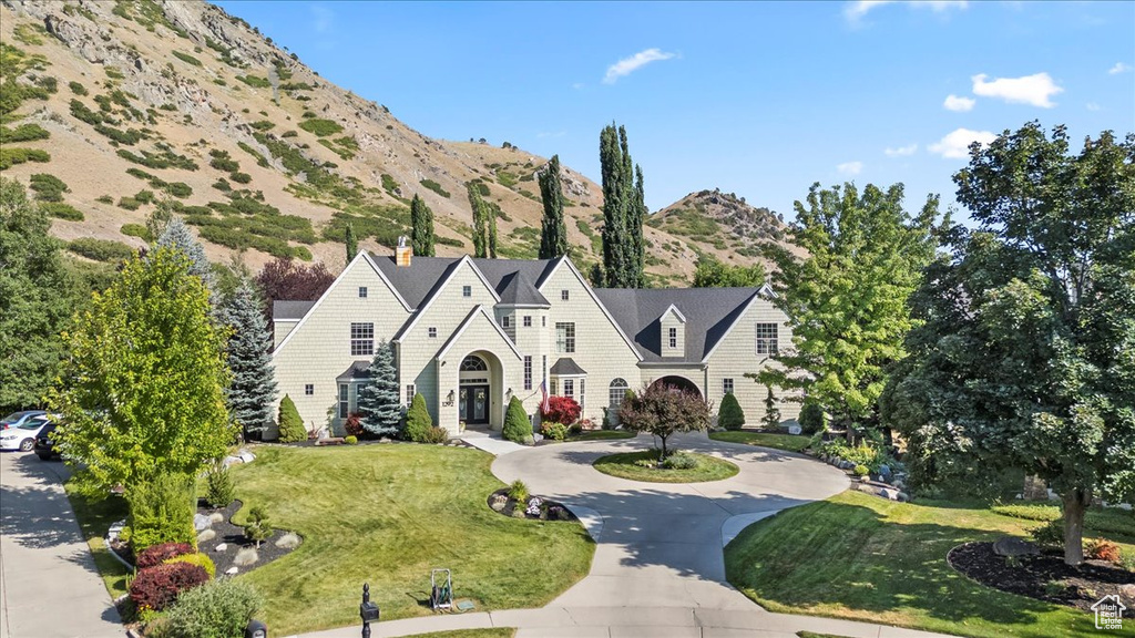 View of front of house featuring a front yard, a mountain view, curved driveway, and a chimney