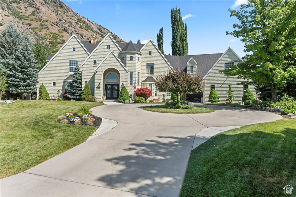 View of front of property featuring french doors, a chimney, a front yard, curved driveway, and a mountain view