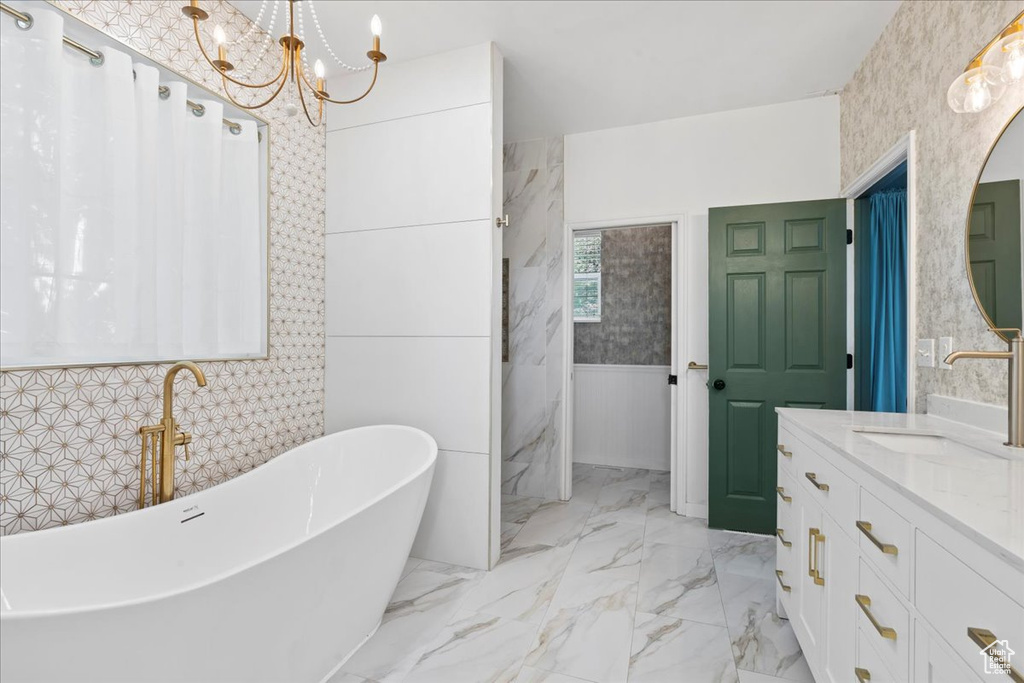 Full bathroom with a freestanding bath, a chandelier, a wainscoted wall, vanity, and wallpapered walls