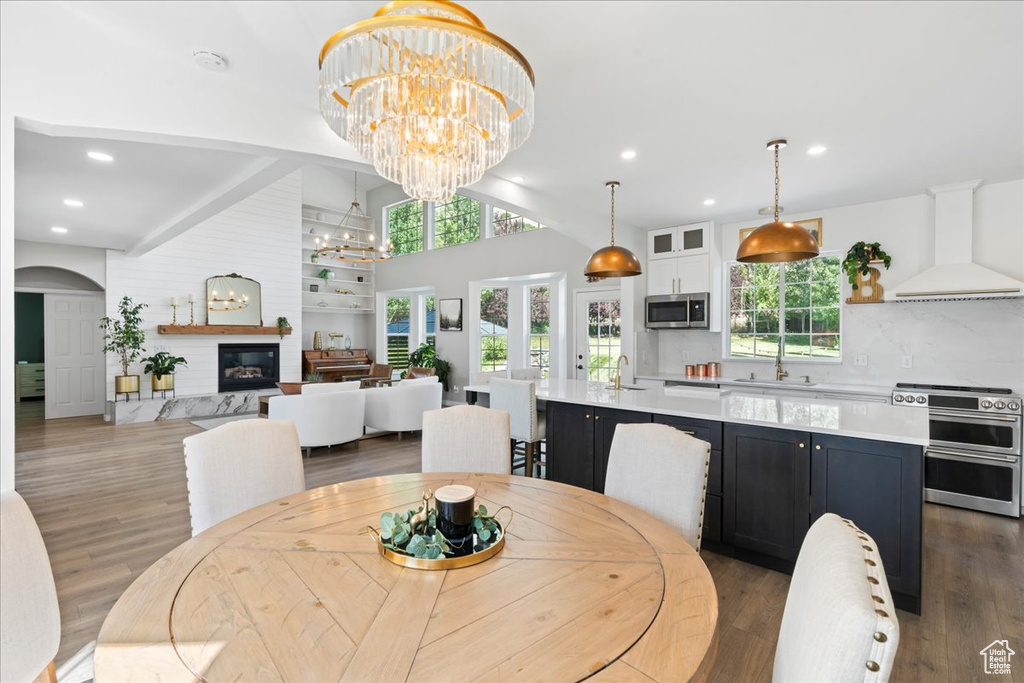 Dining space with a chandelier, wood finished floors, vaulted ceiling, healthy amount of natural light, and a glass covered fireplace