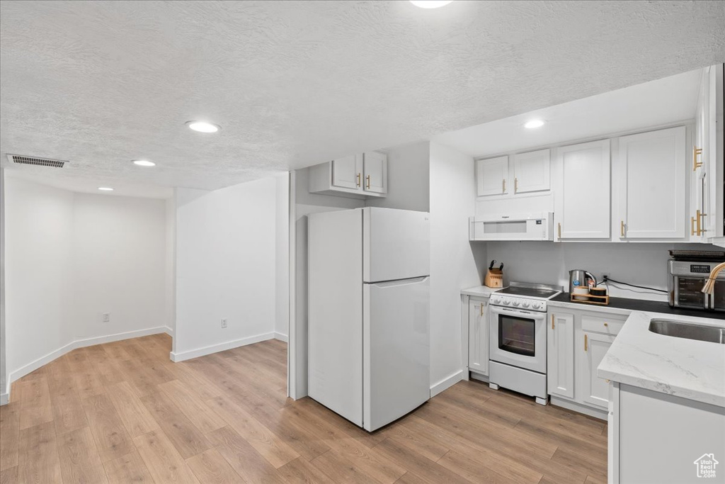 Kitchen with white appliances, recessed lighting, a textured ceiling, light wood-style flooring, and white cabinets