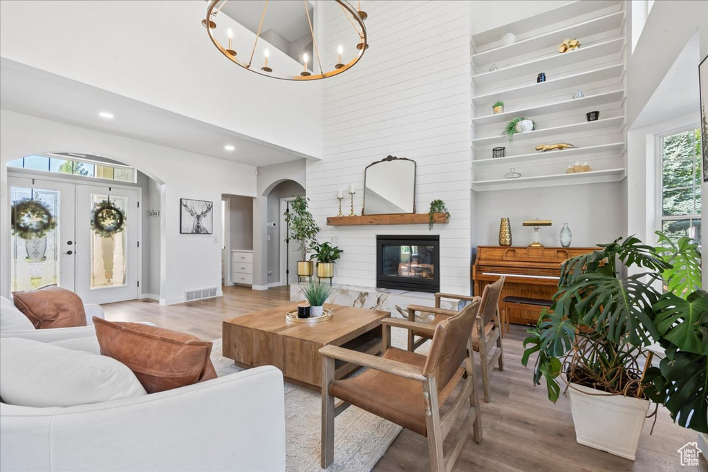 Living area with arched walkways, wood finished floors, a glass covered fireplace, a chandelier, and a towering ceiling