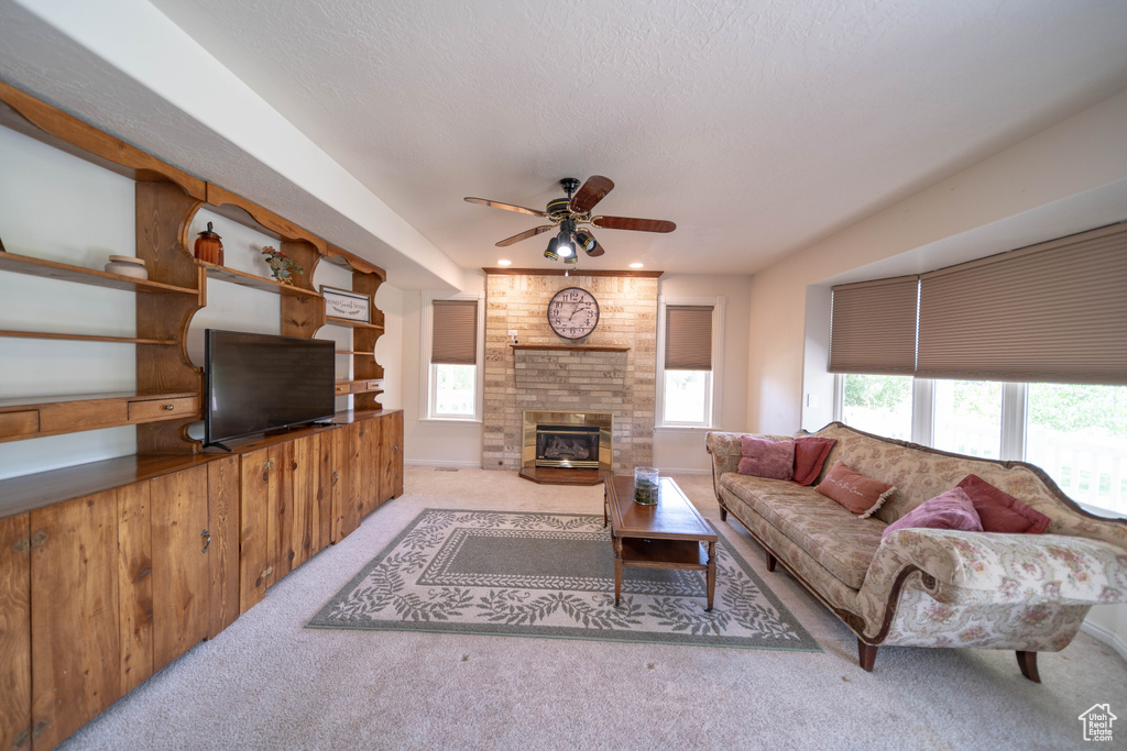 Carpeted living area with a ceiling fan, a large fireplace, and a textured ceiling