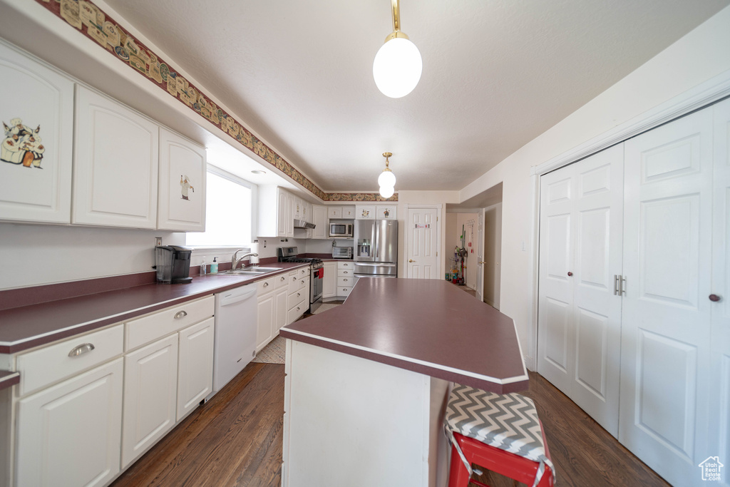 Kitchen with appliances with stainless steel finishes, dark countertops, a center island, and dark wood-style floors