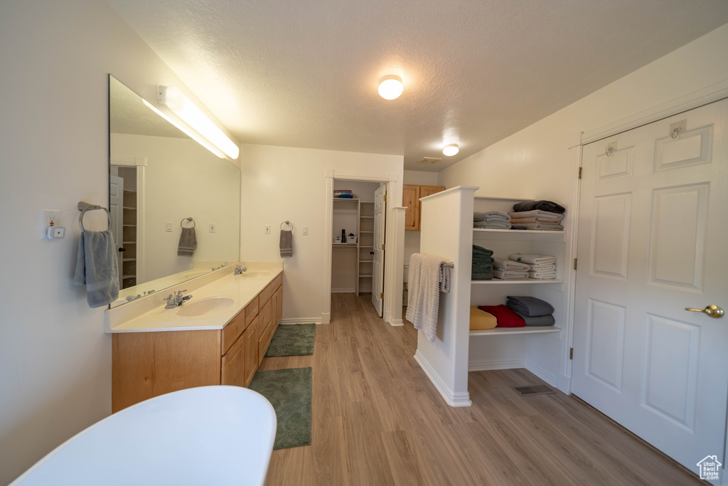 Full bath featuring double vanity, wood finished floors, a textured ceiling, and a walk in closet