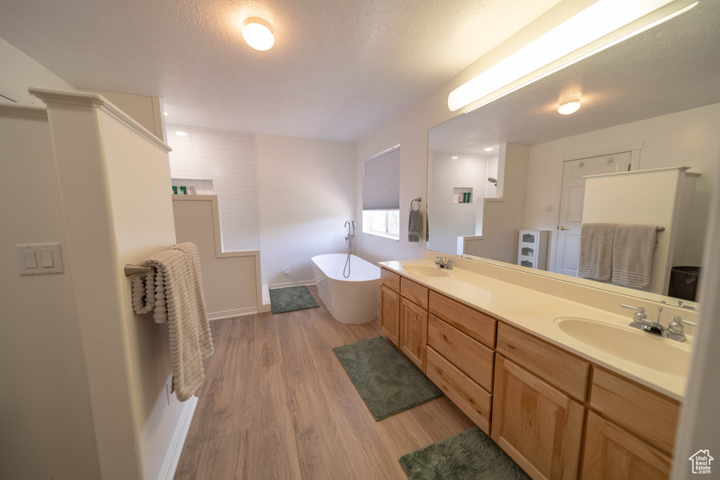 Bathroom with a soaking tub, double vanity, wood finished floors, and a textured ceiling