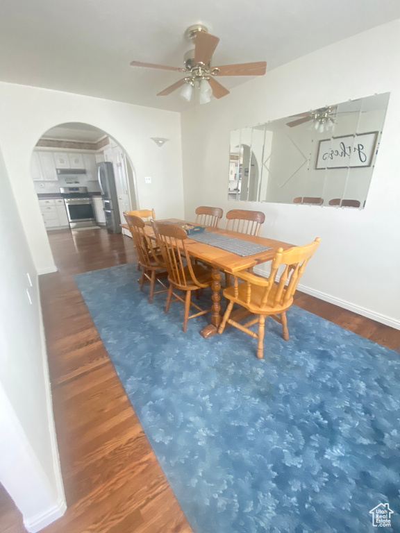 Dining space with arched walkways, wood finished floors, and a ceiling fan