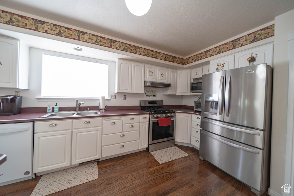 Kitchen featuring appliances with stainless steel finishes, under cabinet range hood, white cabinets, dark wood finished floors, and dark countertops