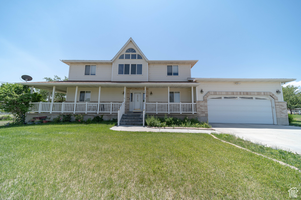 View of front of property featuring an attached garage, driveway, a front lawn, and covered porch