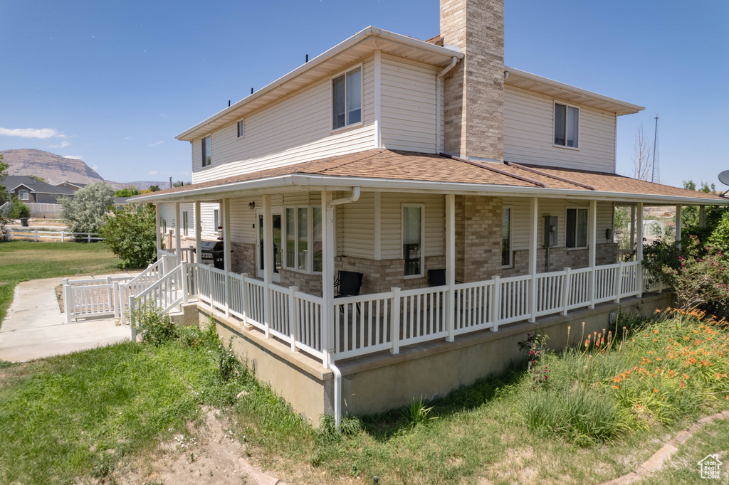 Rear view of house featuring a porch, a chimney, and a shingled roof
