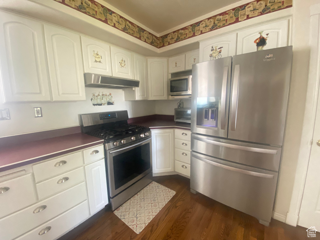 Kitchen with stainless steel appliances, under cabinet range hood, dark countertops, and dark wood-type flooring