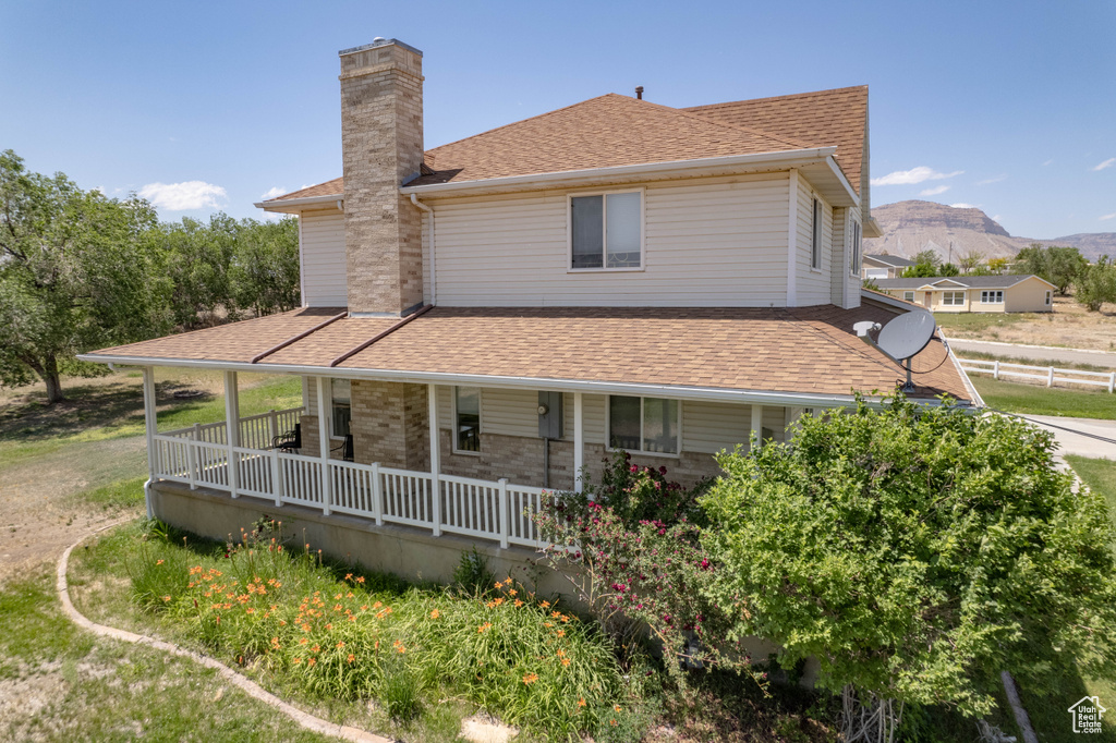 Back of property featuring a chimney, roof with shingles, a porch, and a mountain view