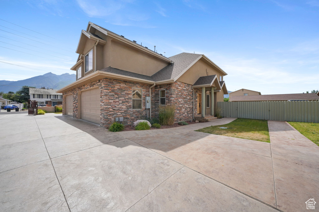 View of front of home featuring an attached garage, a mountain view, concrete driveway, stone siding, and stucco siding