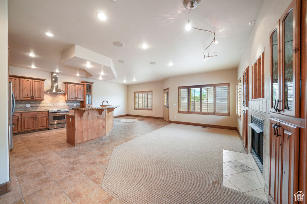 Kitchen with wall chimney exhaust hood, appliances with stainless steel finishes, a breakfast bar area, open floor plan, and a fireplace with flush hearth