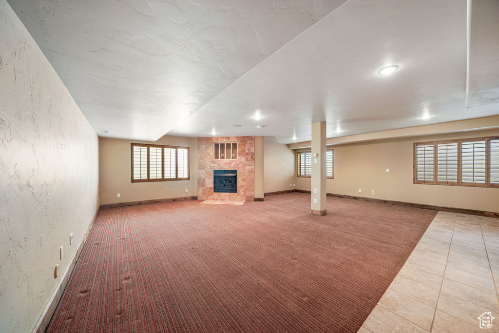 Unfurnished living room featuring a tile fireplace, plenty of natural light, a textured wall, light carpet, and recessed lighting