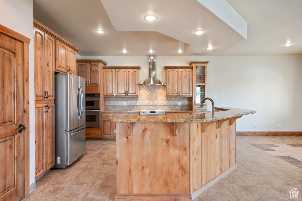 Kitchen with appliances with stainless steel finishes, wall chimney range hood, a breakfast bar, light stone countertops, and recessed lighting