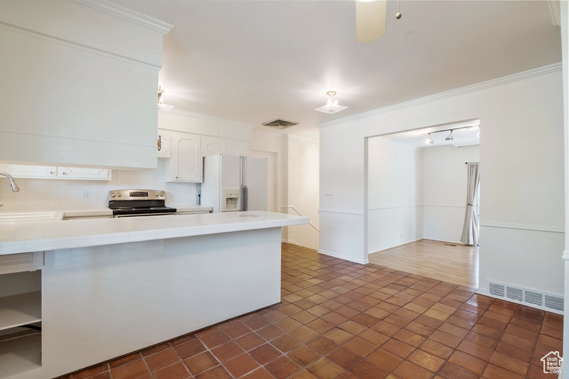 Kitchen featuring white refrigerator with ice dispenser, electric range, tile counters, backsplash, and white cabinets