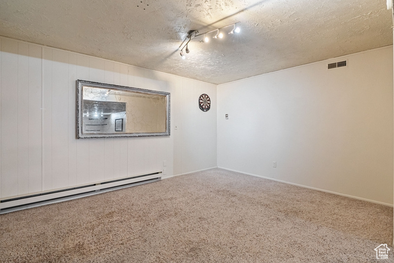Carpeted empty room featuring a textured ceiling and a baseboard radiator