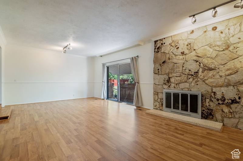 Unfurnished living room with rail lighting, crown molding, a stone fireplace, and wood finished floors
