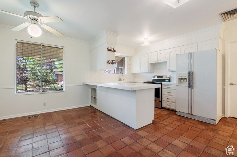 Kitchen featuring white fridge with ice dispenser, stainless steel range with electric stovetop, a peninsula, light countertops, and white cabinets