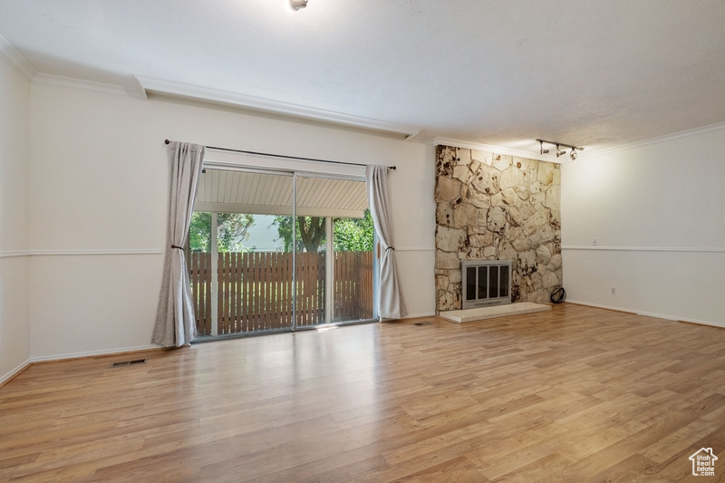 Unfurnished living room featuring crown molding, track lighting, wood finished floors, and a stone fireplace