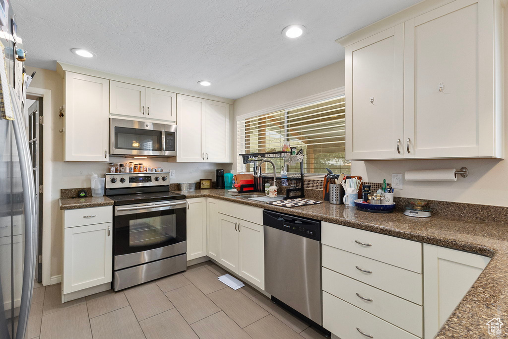 Kitchen with appliances with stainless steel finishes, dark countertops, white cabinetry, recessed lighting, and light tile patterned floors