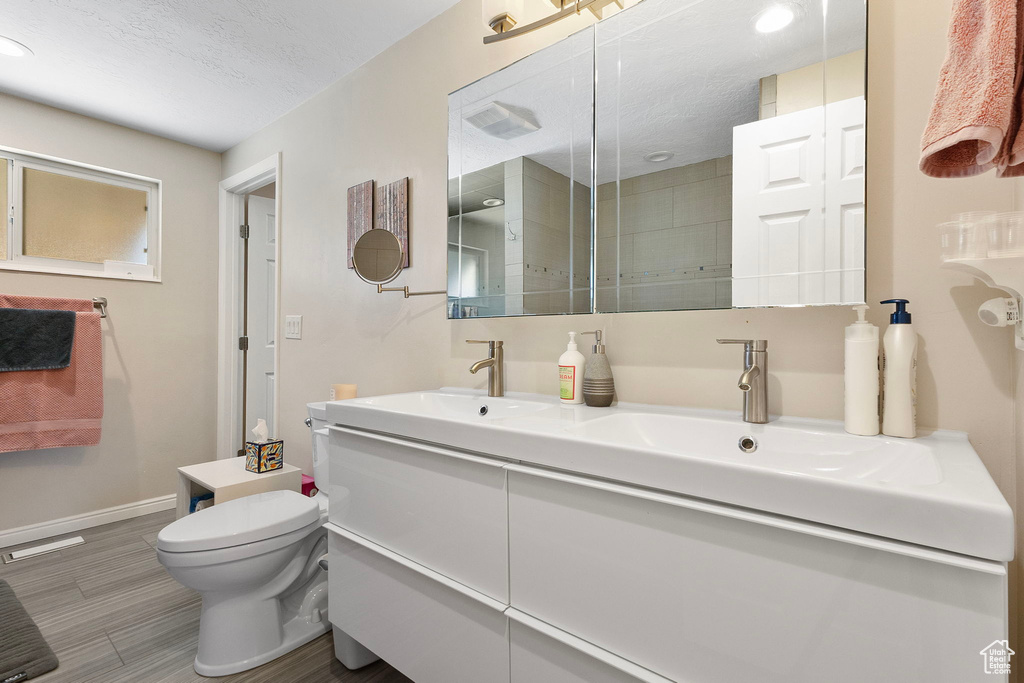 Bathroom featuring double vanity, wood finished floors, tiled shower, and a textured ceiling