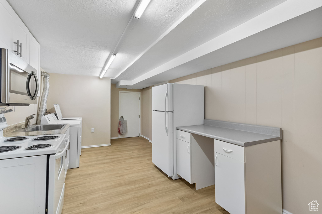 Kitchen featuring white appliances, light wood-type flooring, white cabinetry, light countertops, and independent washer and dryer