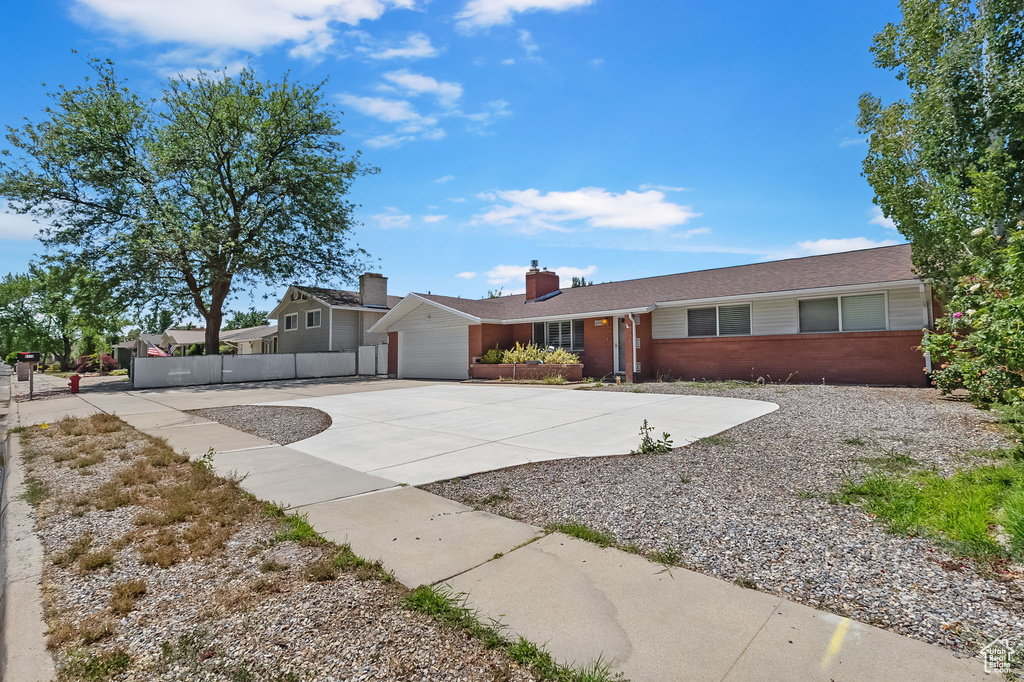 Ranch-style home featuring concrete driveway, brick siding, a chimney, and a garage