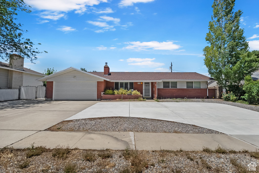 Ranch-style house with concrete driveway, brick siding, a chimney, and a garage