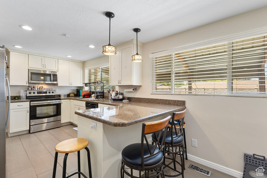 Kitchen with appliances with stainless steel finishes, white cabinets, a peninsula, recessed lighting, and a breakfast bar area