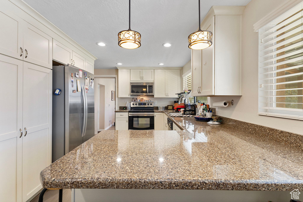 Kitchen featuring stainless steel appliances, recessed lighting, white cabinets, dark stone countertops, and hanging light fixtures