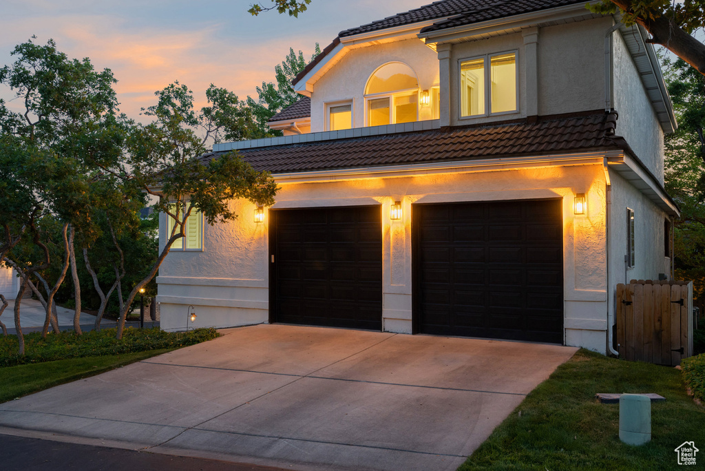 View of front facade with a tile roof, concrete driveway, an attached garage, and stucco siding