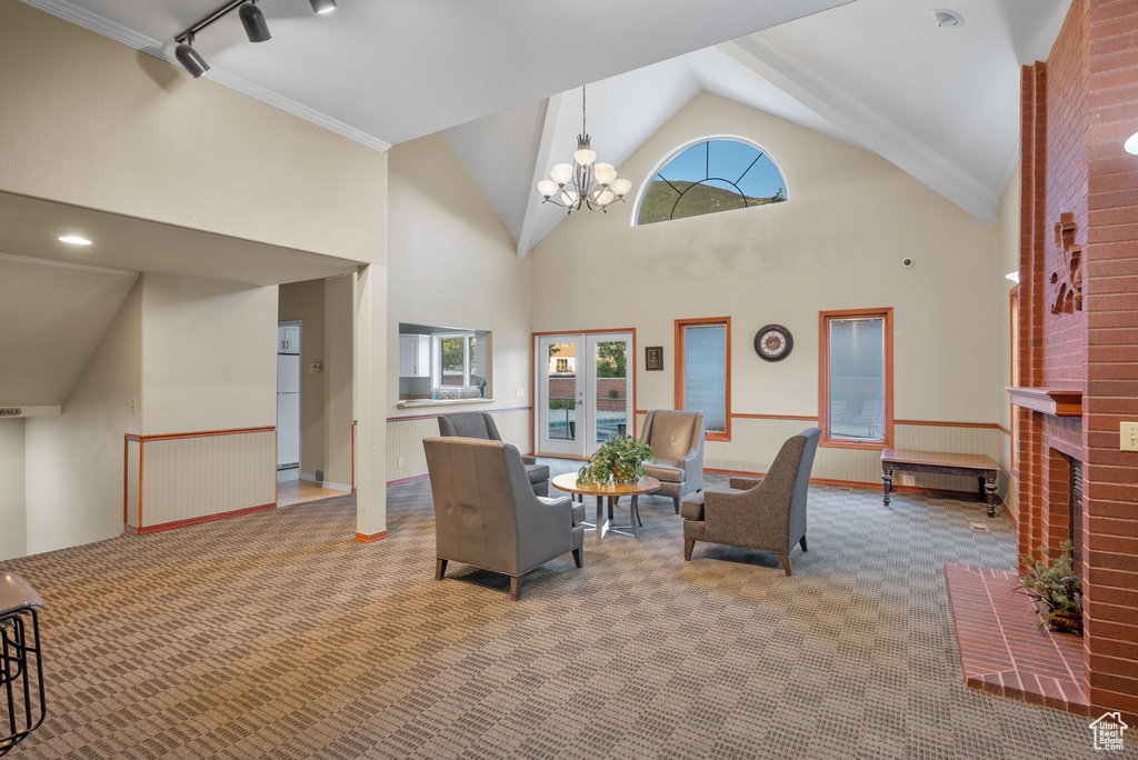Carpeted living area with high vaulted ceiling, a chandelier, a fireplace, and crown molding