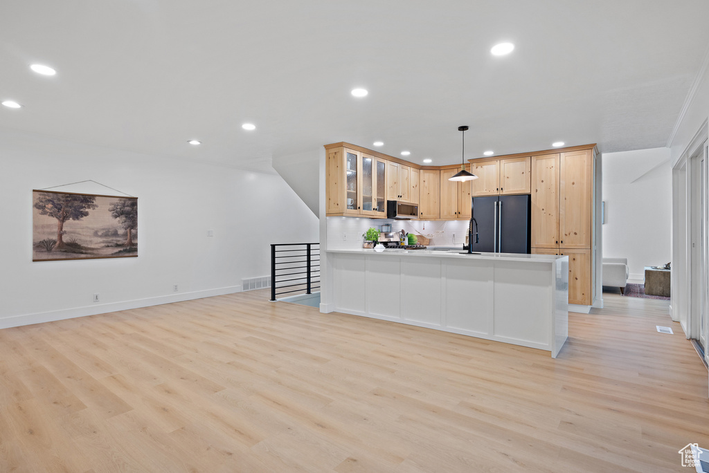 Kitchen with freestanding refrigerator, stainless steel microwave, light wood-style flooring, glass insert cabinets, and a peninsula