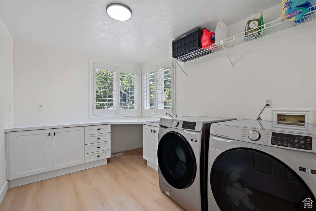Laundry room featuring washer and dryer, cabinet space, light wood-type flooring, and a textured ceiling
