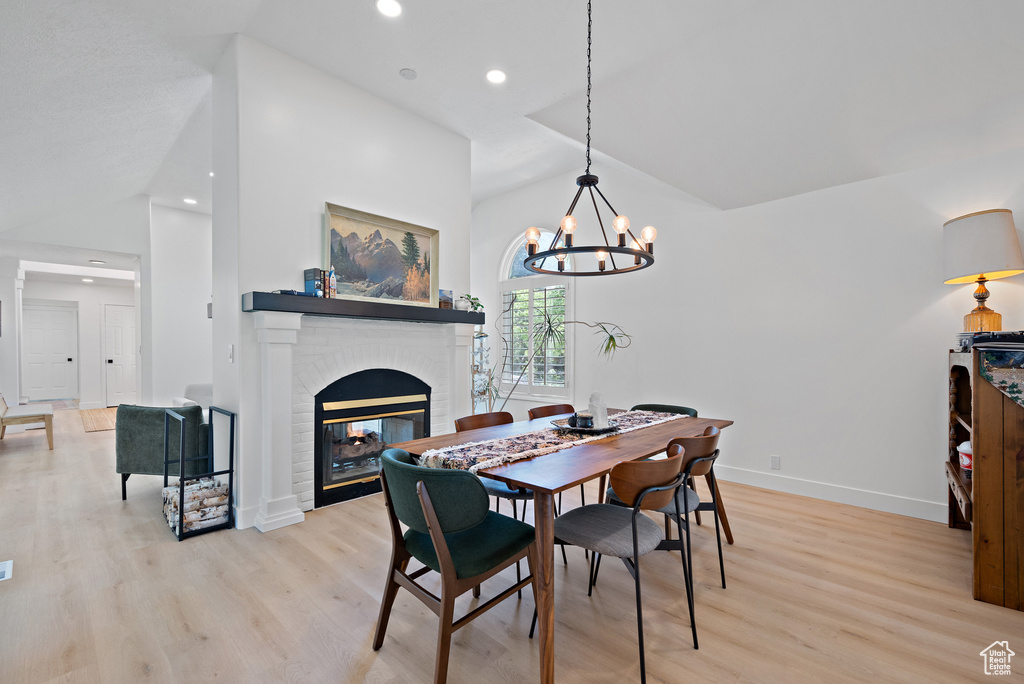 Dining area with lofted ceiling, light wood-style floors, a fireplace, a chandelier, and recessed lighting