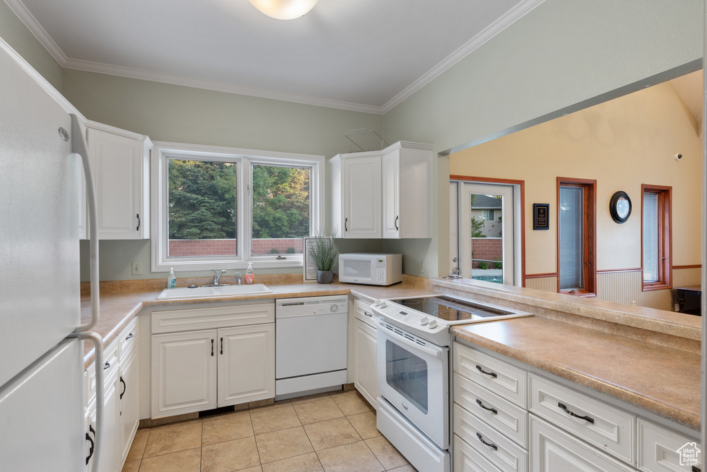 Kitchen with white appliances, light tile patterned flooring, white cabinets, crown molding, and light countertops