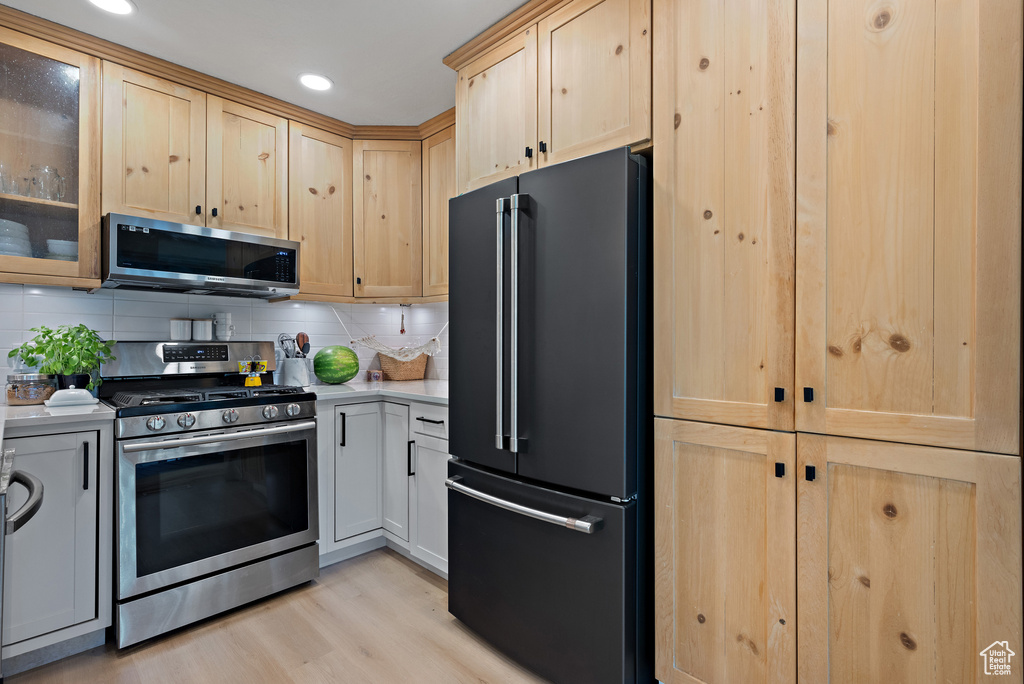 Kitchen with stainless steel appliances, light brown cabinets, light countertops, light wood-style flooring, and tasteful backsplash
