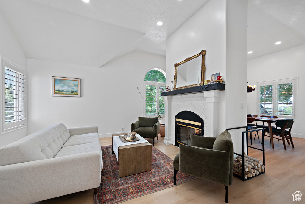 Living area featuring vaulted ceiling, plenty of natural light, a fireplace, wood finished floors, and recessed lighting