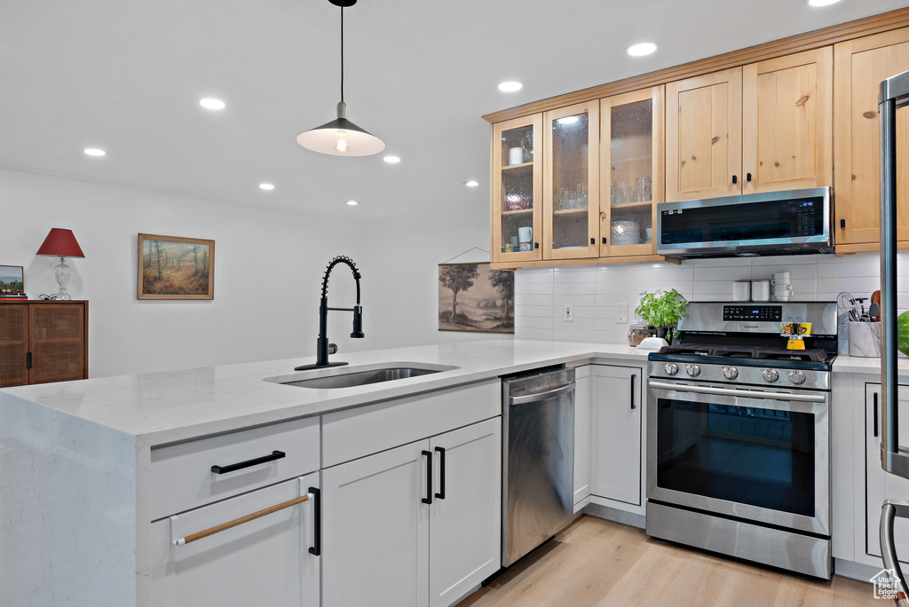 Kitchen featuring appliances with stainless steel finishes, a peninsula, decorative backsplash, light stone countertops, and light wood finished floors